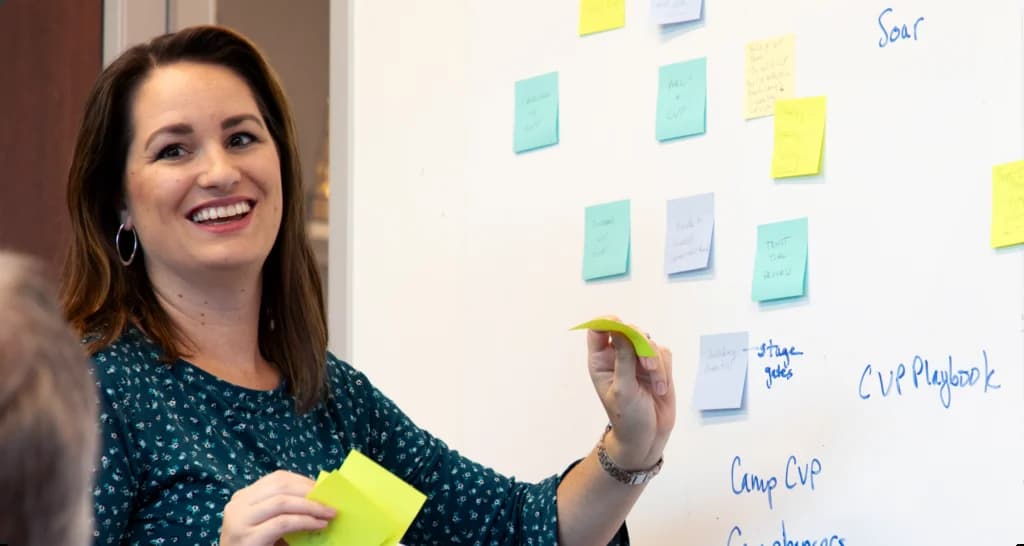 a woman standing in front of a whiteboard with sticky notes on it