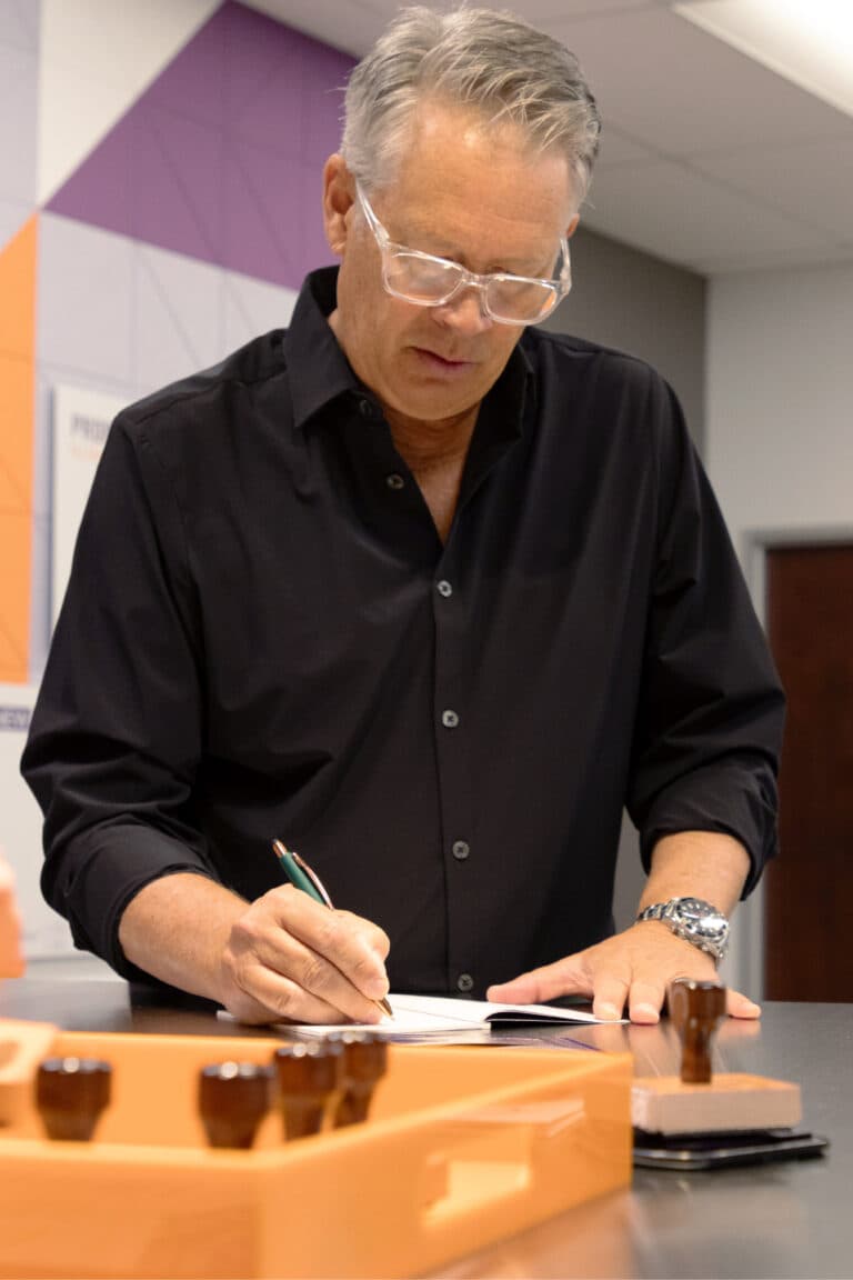 a man in a black shirt writing on a piece of wood