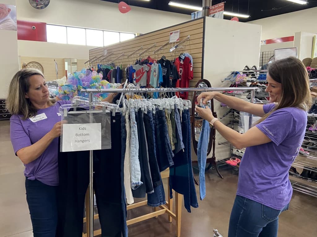 a couple of women standing in front of a rack of shirts