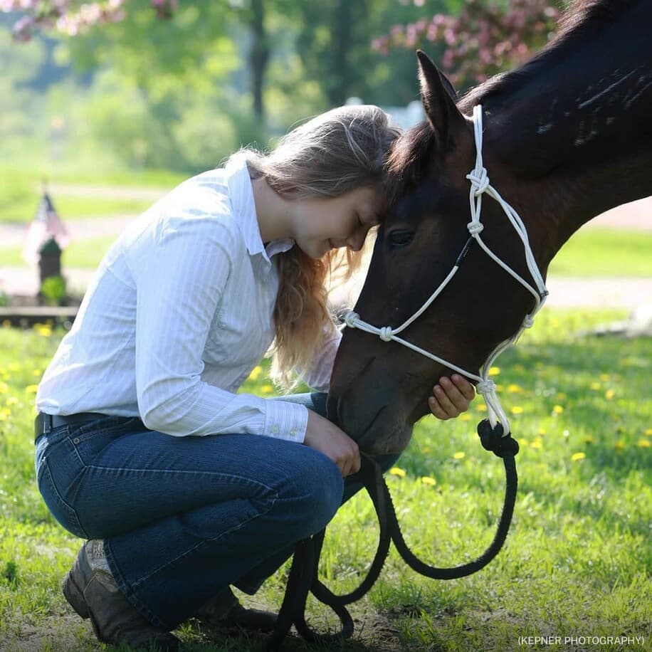 A woman kneeling down to pet a horse